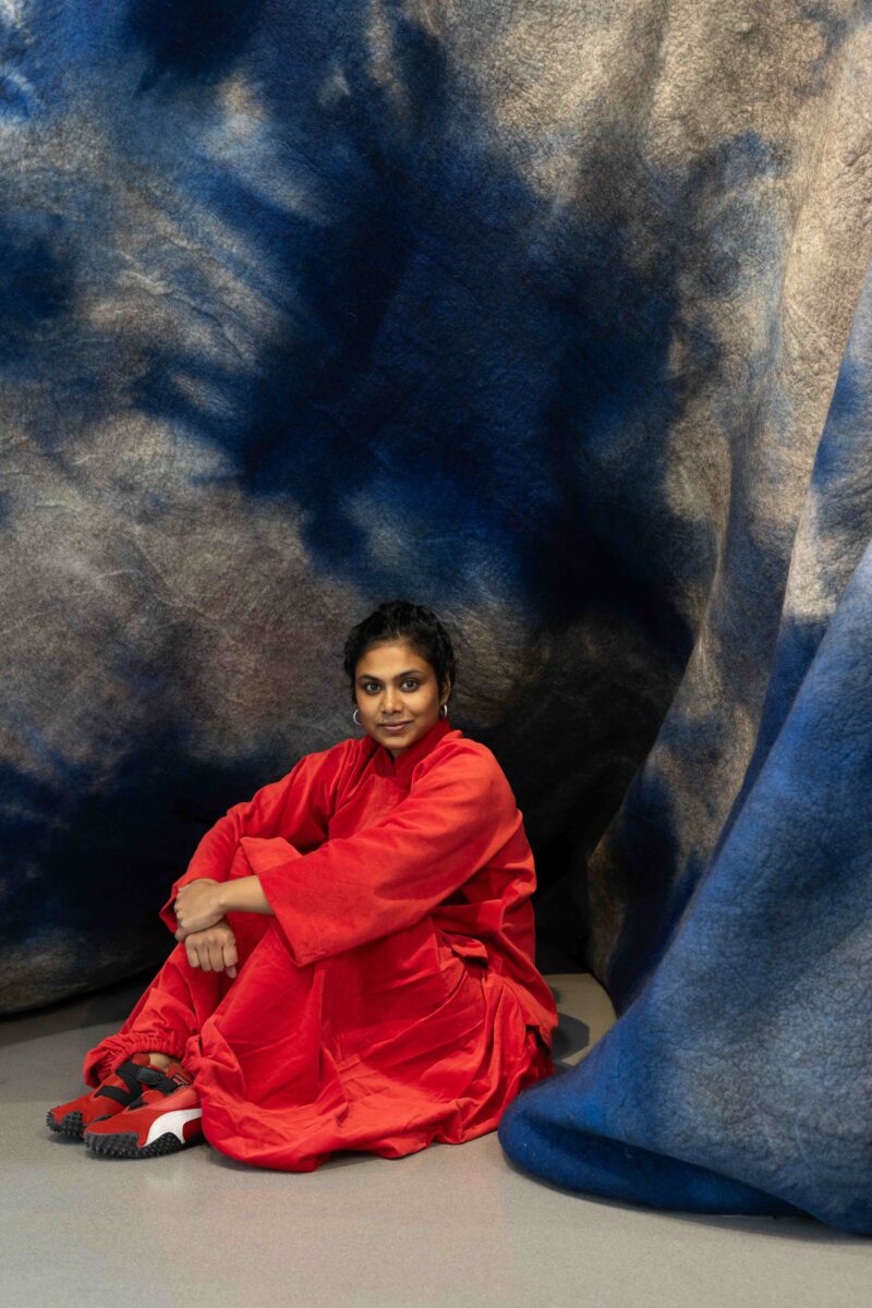 Artist Sagarika Sundaram sits with her work Blue Mountain 2026 in her exhibition Reservoir at Henry Moore Institute. Courtesy the artist, Henry Moore Institute and Alison Jacques, London Photo: Rob Harris